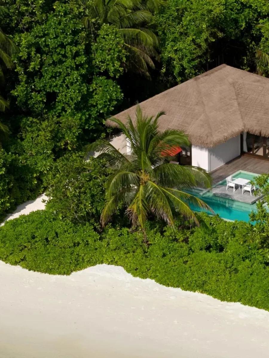 A Beach Villa at Noku Maldives seen from above, its thatched roof and private pool set among palms just off the sand