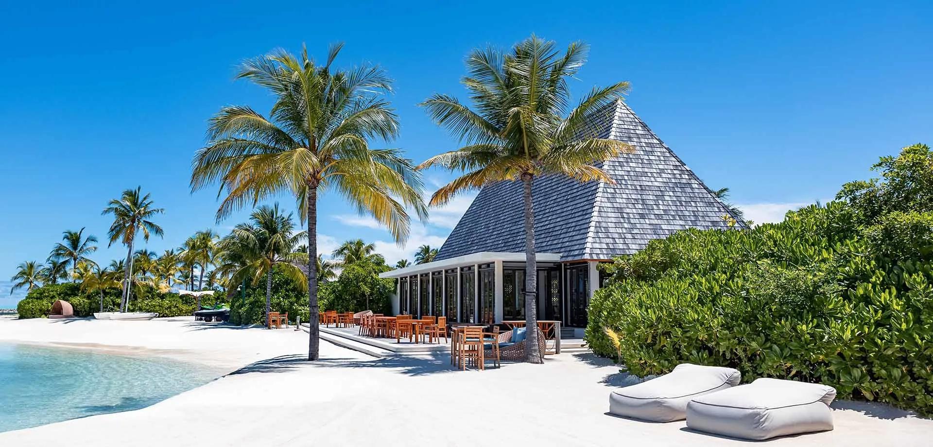 Mar-Umi's beachfront terrace at Kuda Villingili Resort Maldives, tables set beneath palms by the lagoon