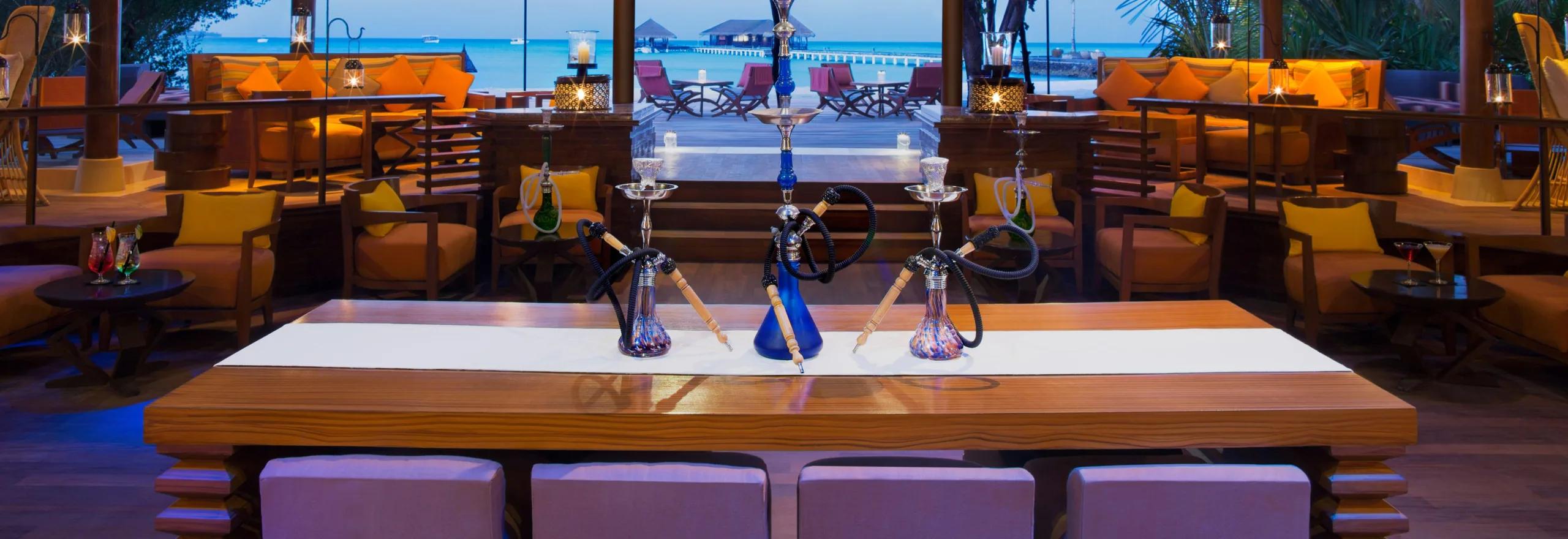 Equator Bar & Lounge in the evening, shisha pipes set on the central table and the overwater jetty visible through the open sides