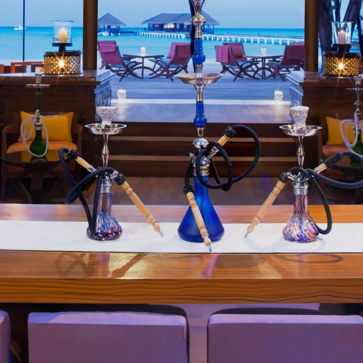 Equator Bar & Lounge in the evening, shisha pipes set on the central table and the overwater jetty visible through the open sides