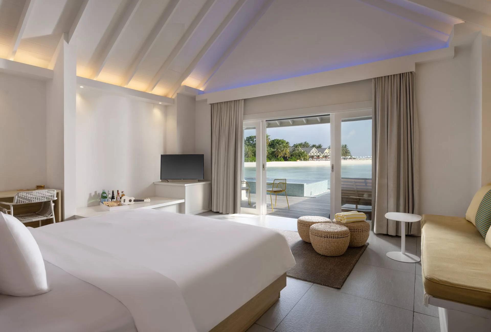 The bedroom of a Lagoon Overwater Villa at The Standard, glass doors opening onto a deck and plunge pool above the lagoon