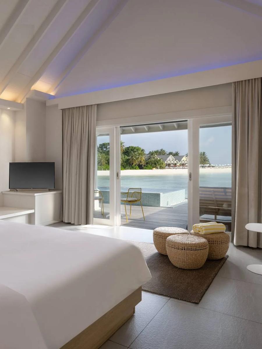 The bedroom of a Lagoon Overwater Villa at The Standard, glass doors opening onto a deck and plunge pool above the lagoon