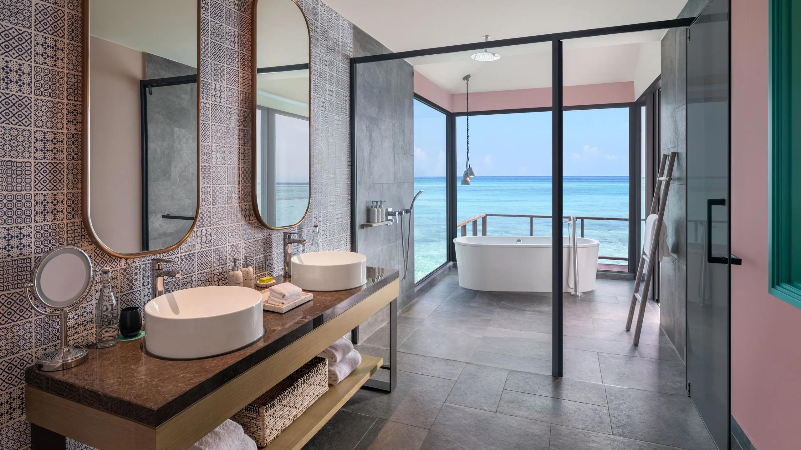 The overwater bathroom of a Sunrise Overwater Villa, with a freestanding tub set against the lagoon view