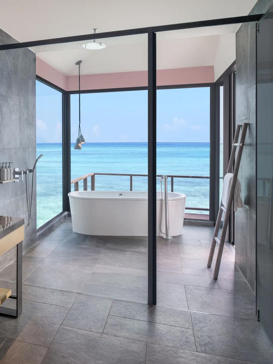The overwater bathroom of a Sunrise Overwater Villa, with a freestanding tub set against the lagoon view
