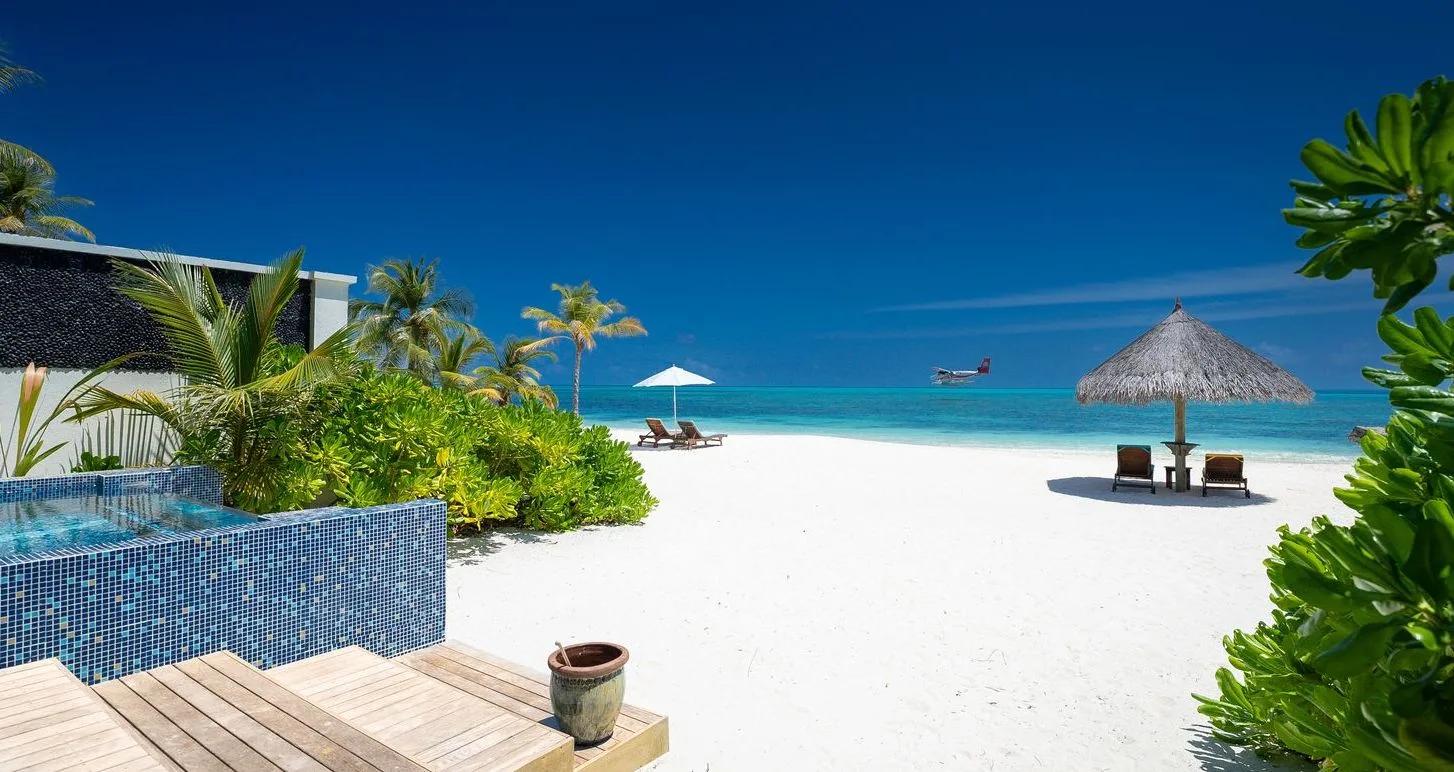 A private pool deck at Atmosphere Kanifushi, a seaplane arriving over the lagoon beyond