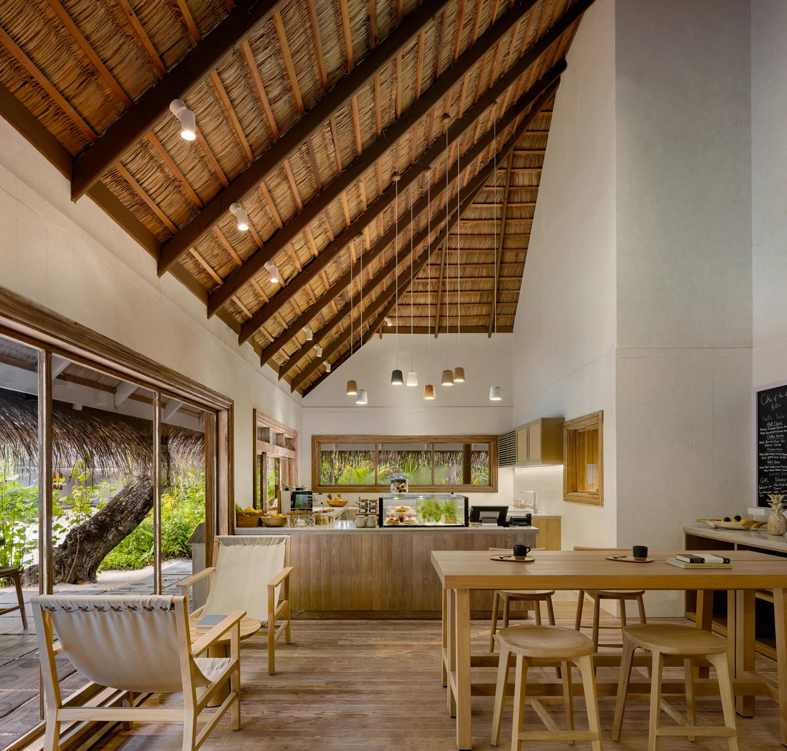 The high thatched-roof interior of Scoops, with a pastry display case, chalkboard menu, and communal wooden dining tables.