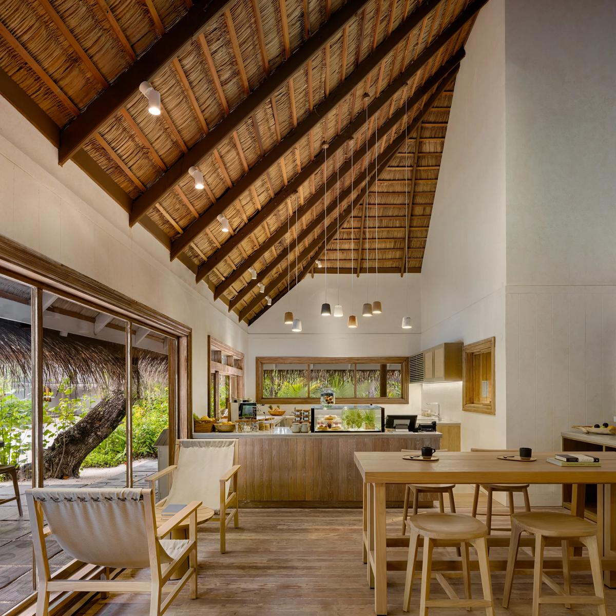 The high thatched-roof interior of Scoops, with a pastry display case, chalkboard menu, and communal wooden dining tables.