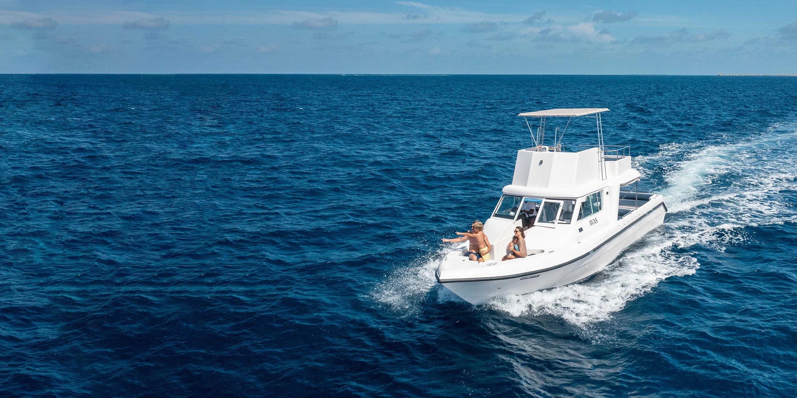 A Baglioni Maldives excursion yacht underway with a family seated at the bow, the island visible astern