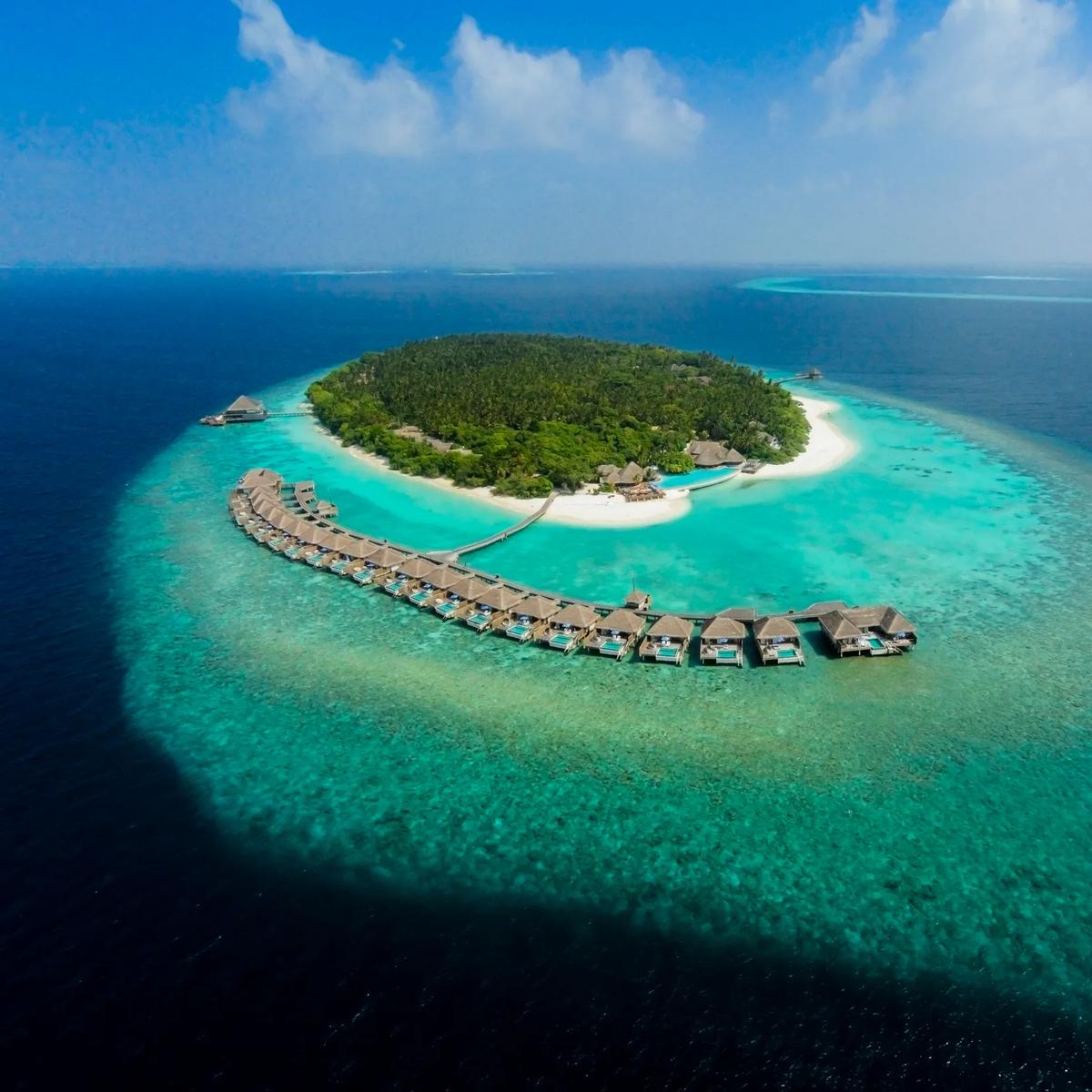 Aerial view of Dusit Thani Maldives' overwater villa row curving along the reef edge on Mudhdhoo Island, Baa Atoll