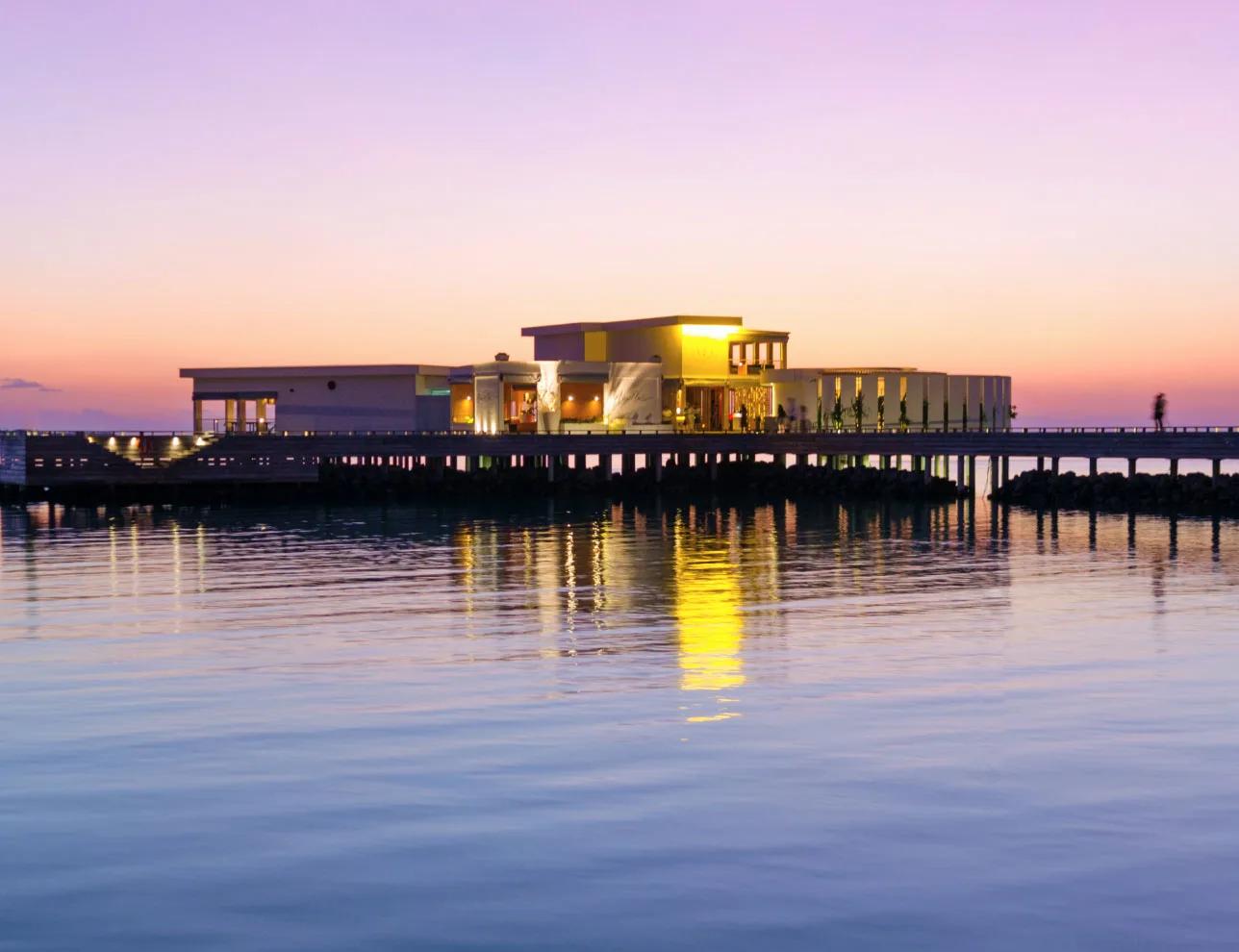 Feeling Koi's overwater dining room at Amilla lit up at dusk, reached by its own jetty