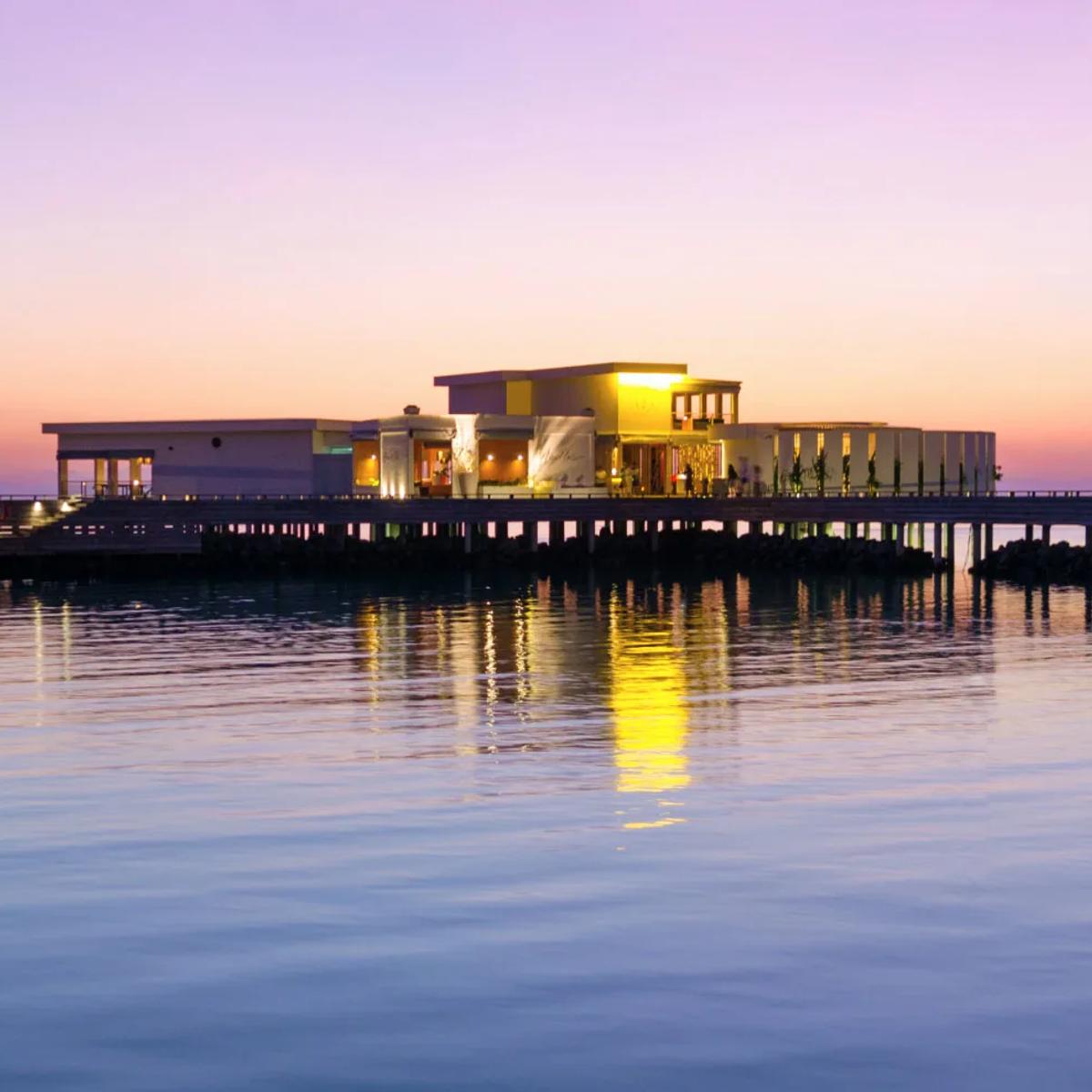 Feeling Koi's overwater dining room at Amilla lit up at dusk, reached by its own jetty