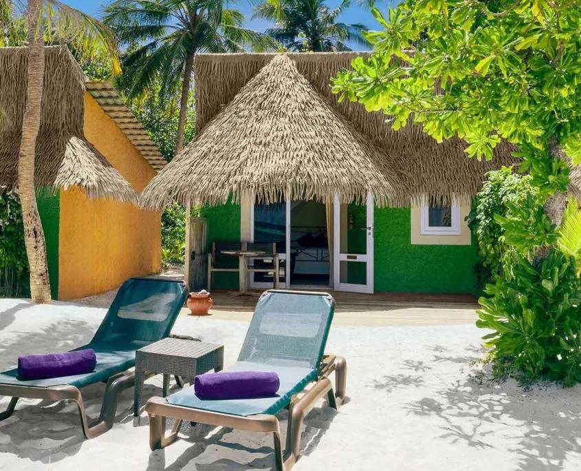 Premium Beach Bungalow's green-and-yellow exterior beneath a thatched roof, with sun loungers on the sand