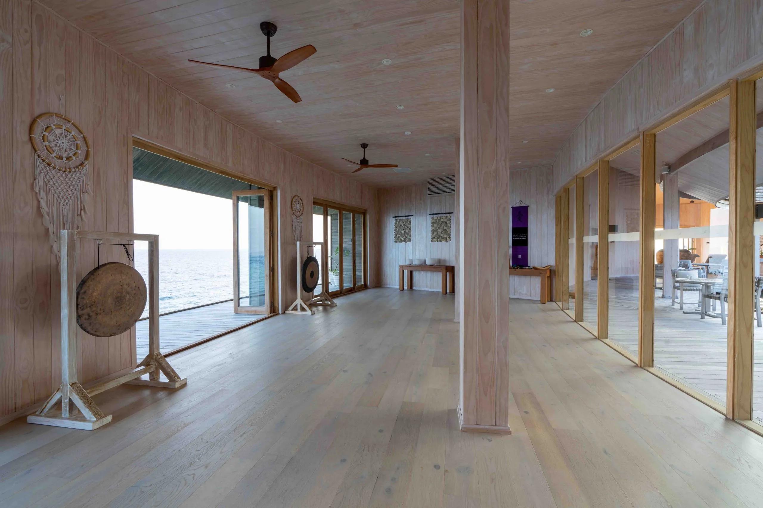 Two gongs mounted on wooden stands inside the Yoga Studio, glass doors open to the ocean beyond