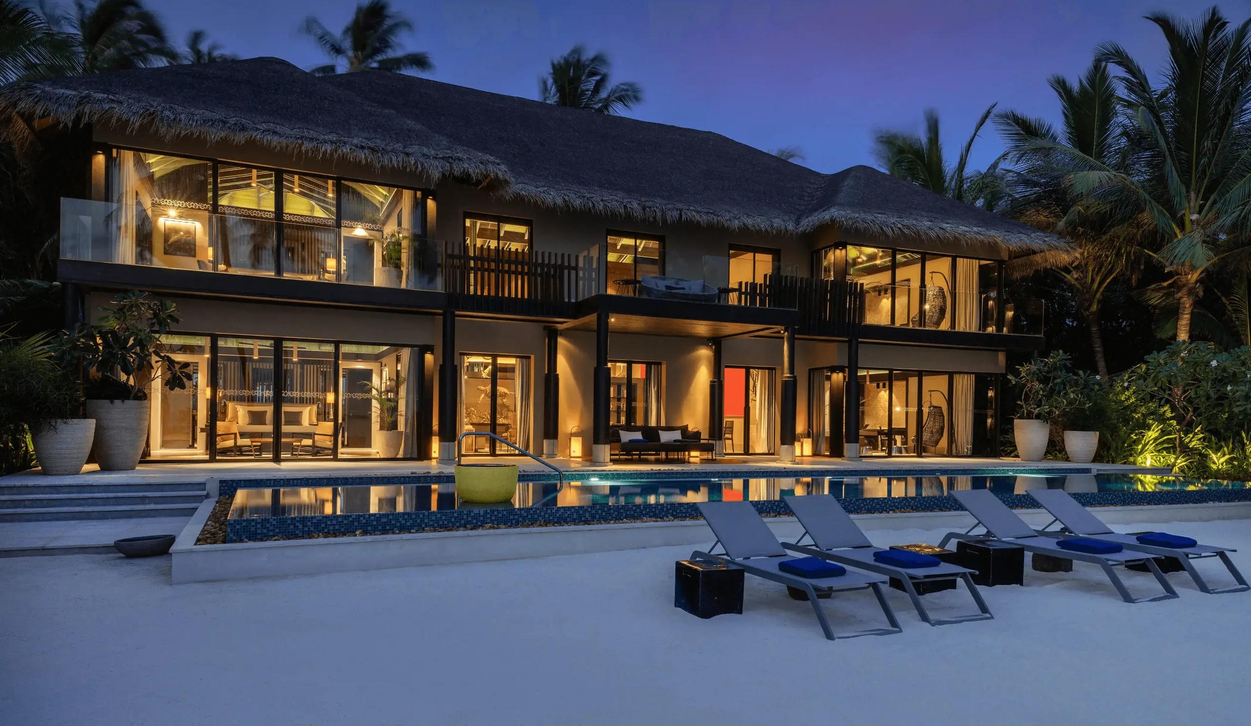 Funa Private Residence's pool and beach terrace lit at dusk, palm trees rising beside the two-storey building