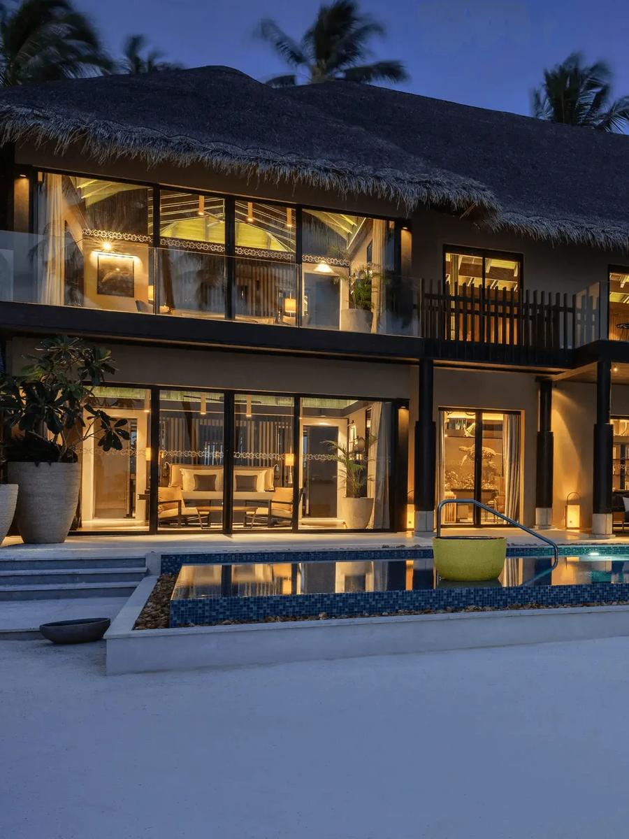 Funa Private Residence's pool and beach terrace lit at dusk, palm trees rising beside the two-storey building