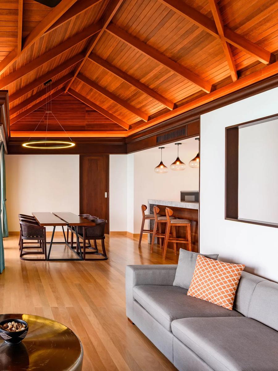 Living and dining area of the Two-Bedroom Overwater Villa With Pool, with a dining table, sofa and breakfast bar under a vaulted wood ceiling