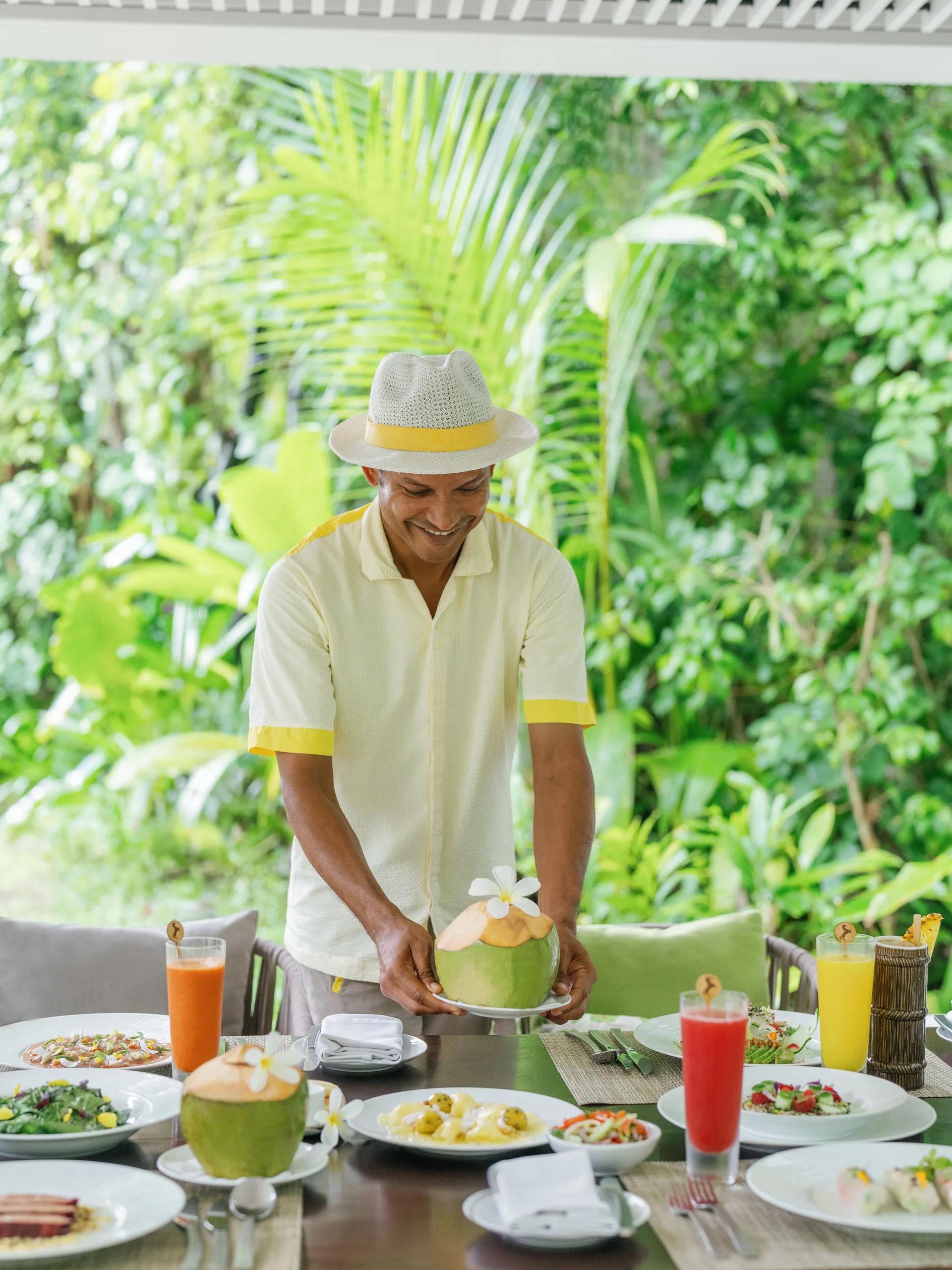 A tropical lunch spread of ceviche, coconuts and noodles set on a villa terrace table surrounded by palms