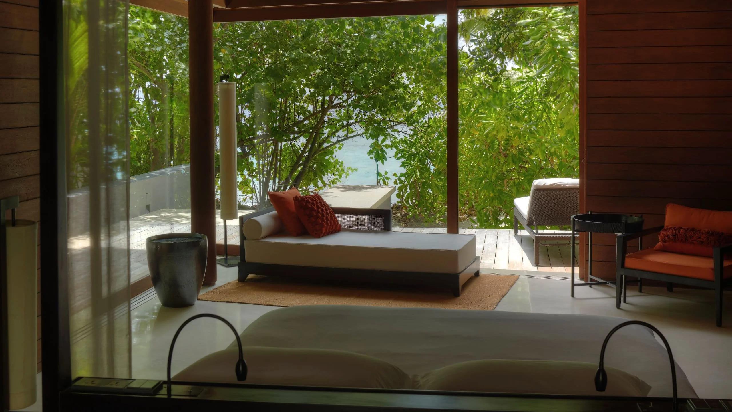A daybed on the private deck of a Beach Villa, screened by trees with the lagoon visible beyond