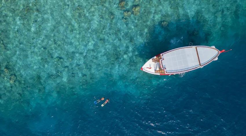 A snorkelling dhoni anchored over the house reef, two guests swimming in the water below