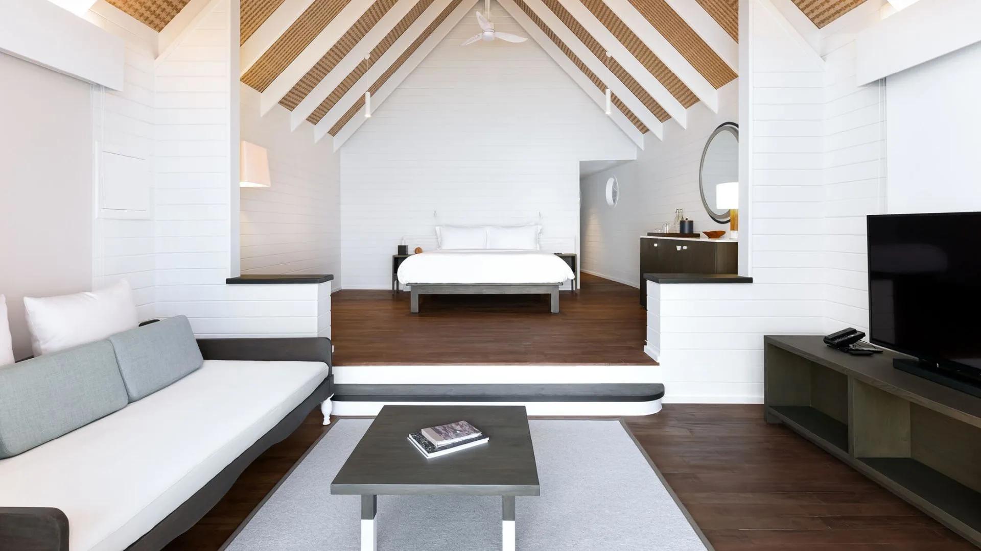 The vaulted, dhoni-boat-shaped interior of a Dhoni Water Villa, with a raised bedroom platform beneath exposed timber rafters