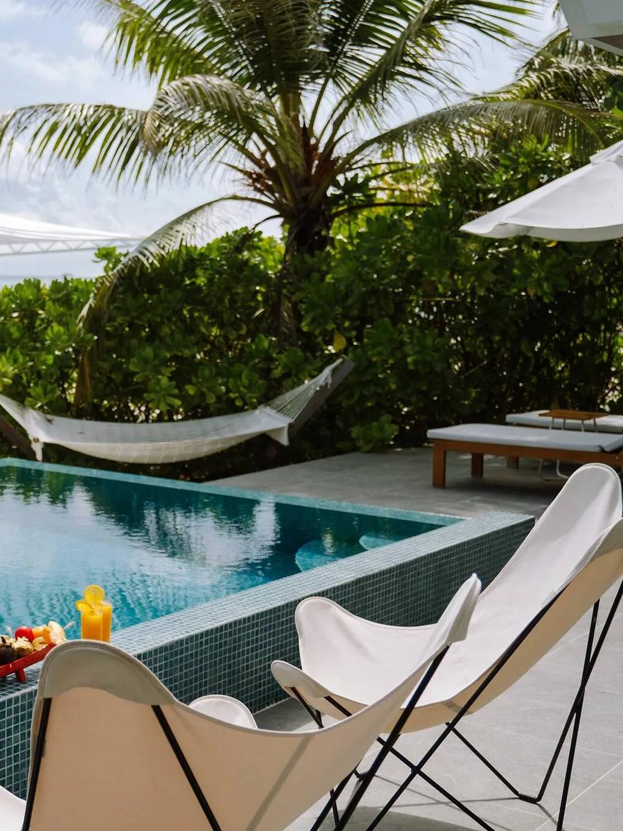 A private pool deck at a Two Bedroom Ocean Beach Villa with a hammock and a fruit-topped breakfast tray poolside, the beach beyond