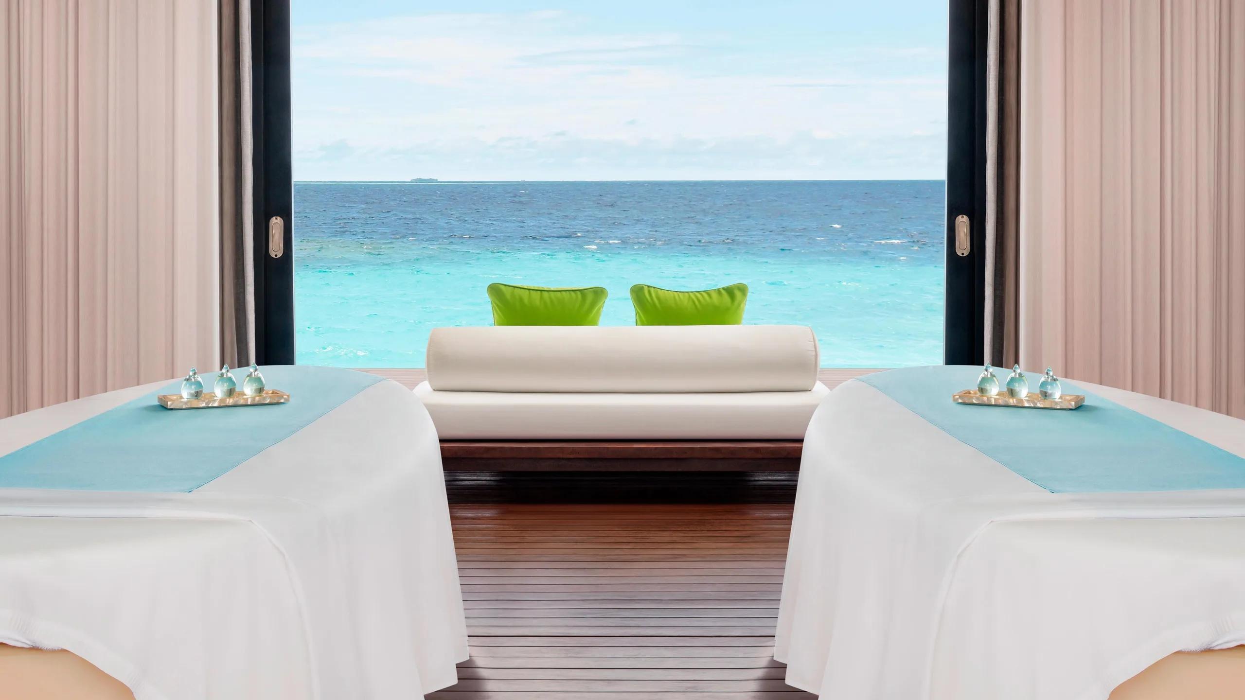 A treatment room at AWAY Spa, with two massage tables and a daybed facing an open deck over the ocean