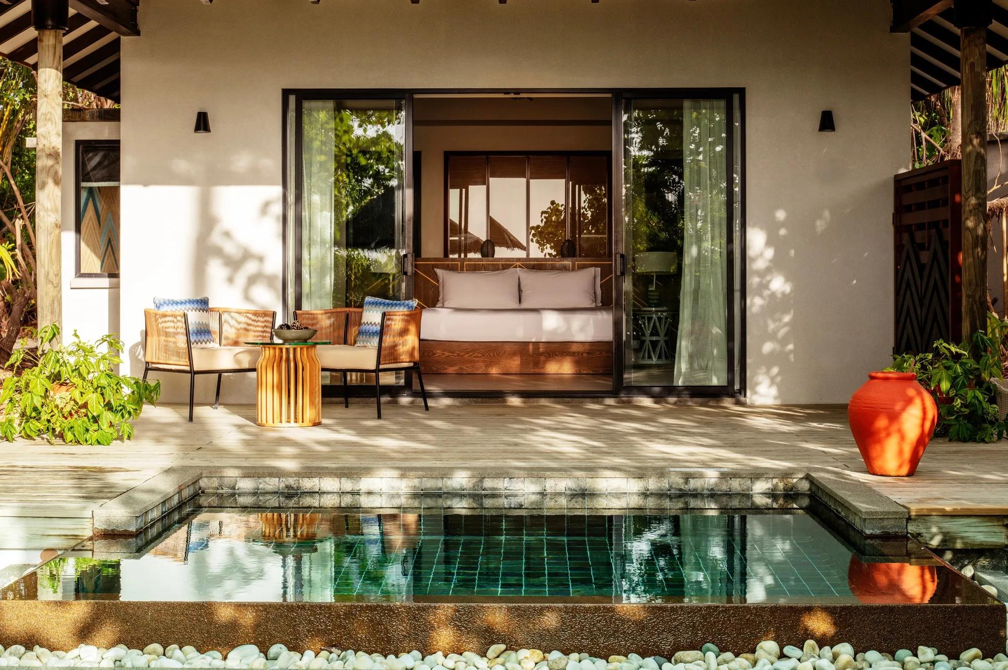A Sunrise Beach Pool Villa's bed beside a window looking onto its private pool and a thatched umbrella outside