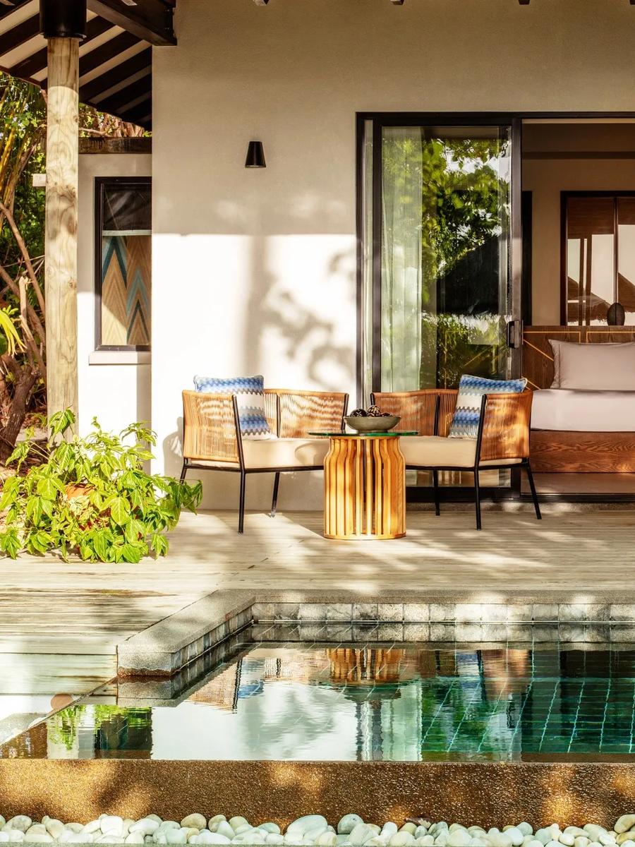 A Sunrise Beach Pool Villa's bed beside a window looking onto its private pool and a thatched umbrella outside