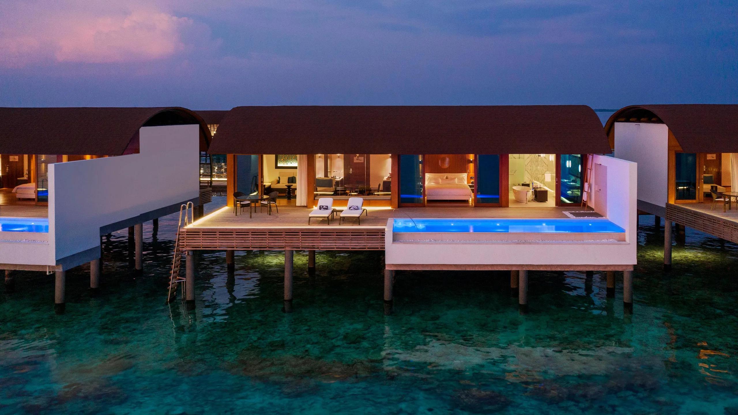 A Heavenly Overwater Villa with Pool at dusk, its infinity pool lit blue above the reef