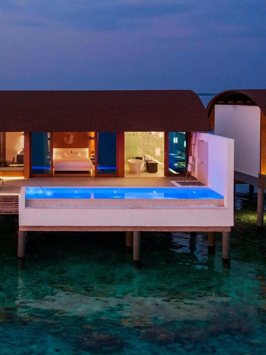 A Heavenly Overwater Villa with Pool at dusk, its infinity pool lit blue above the reef