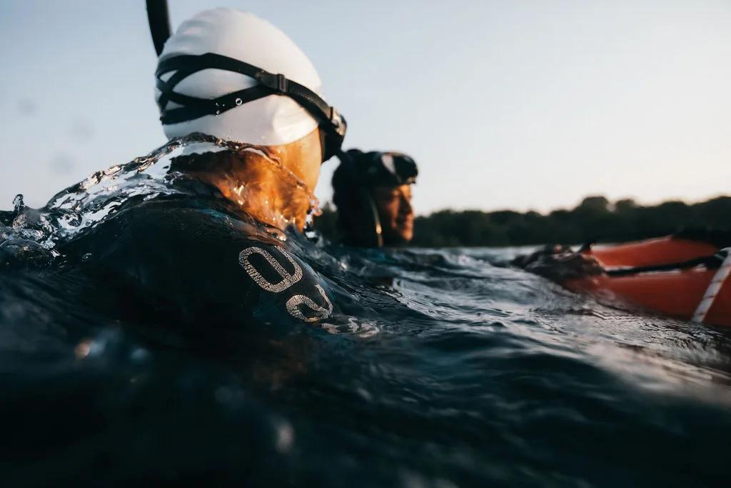 Two freedivers surface side by side in open water, masks and snorkels on, a support buoy floating nearby