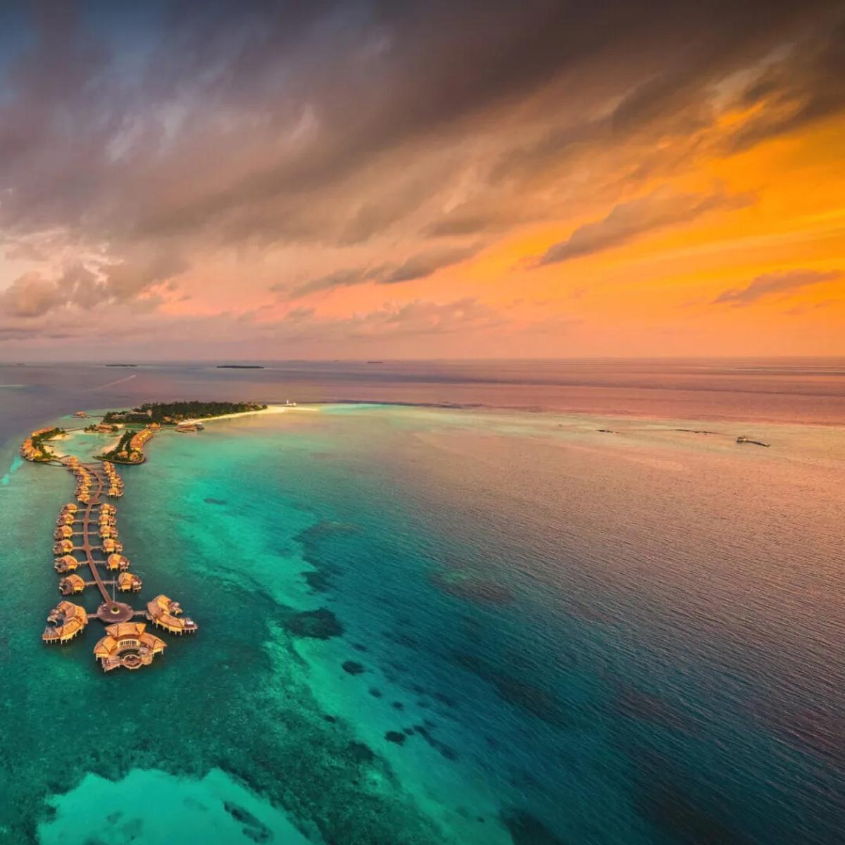 Aerial view at dusk of InterContinental Maldives Maamunagau's overwater villas extending in a line from the island into the Raa Atoll lagoon