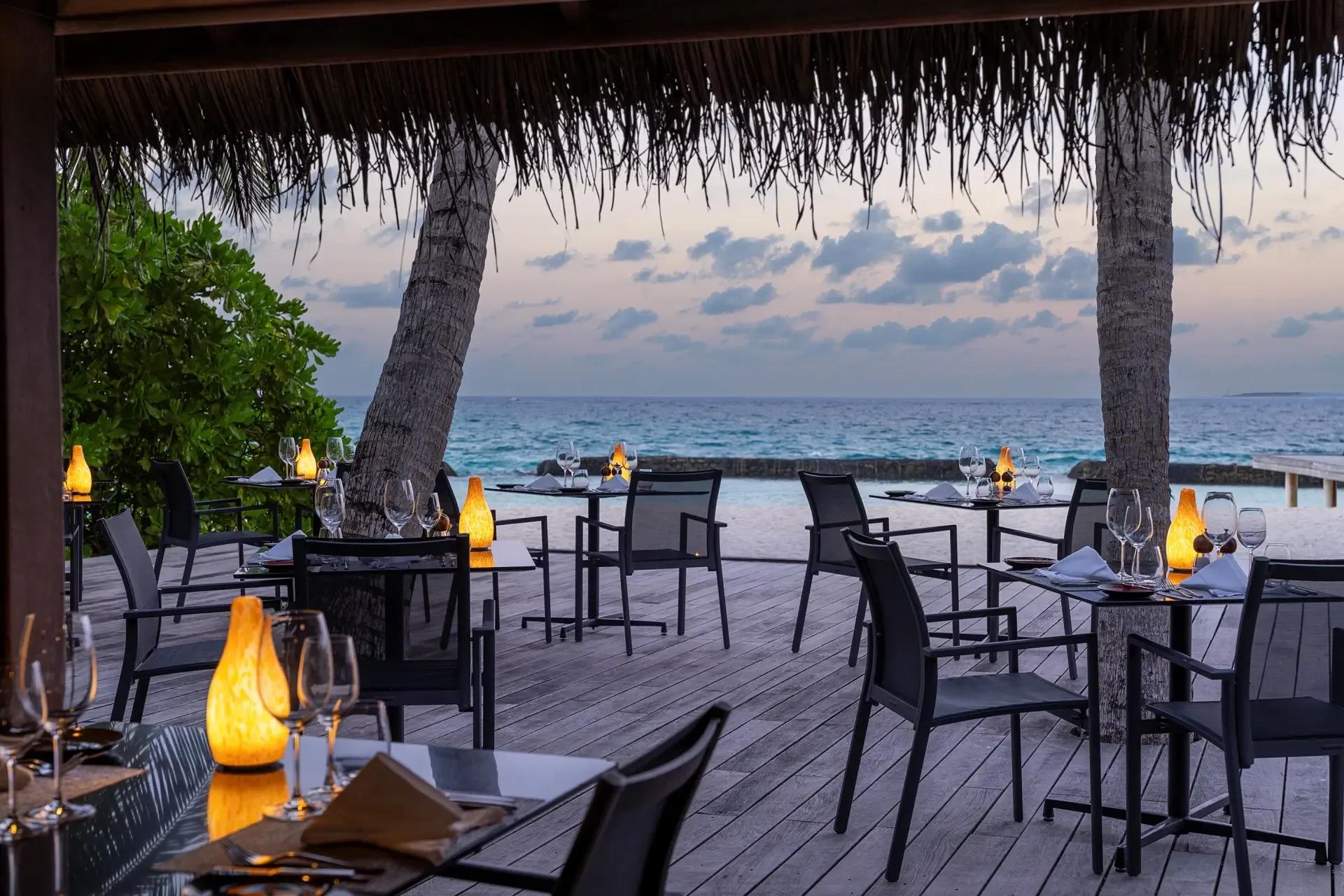 Island Barbeque's beachfront dining tables at dusk, palm trees and the open ocean beyond