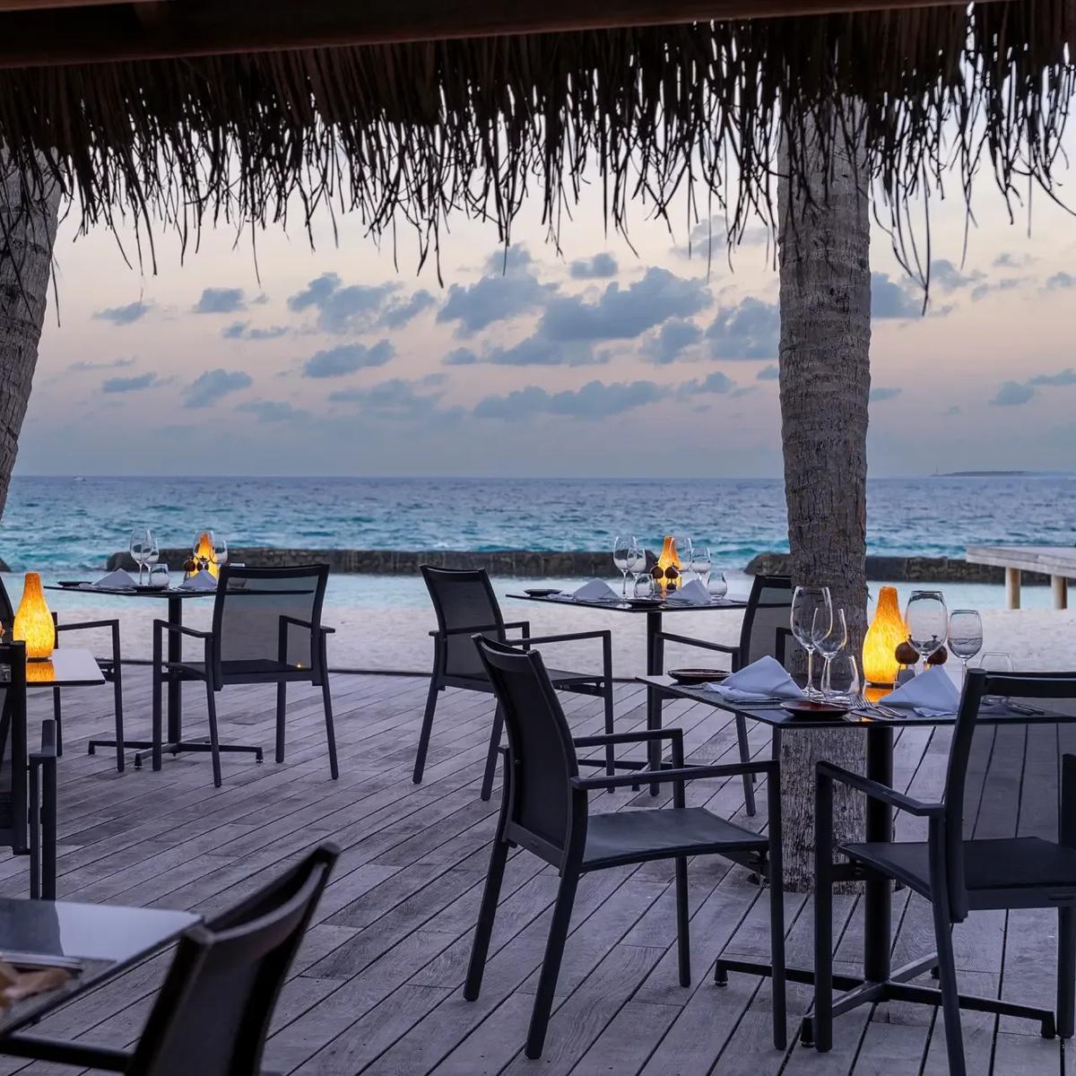 Island Barbeque's beachfront dining tables at dusk, palm trees and the open ocean beyond