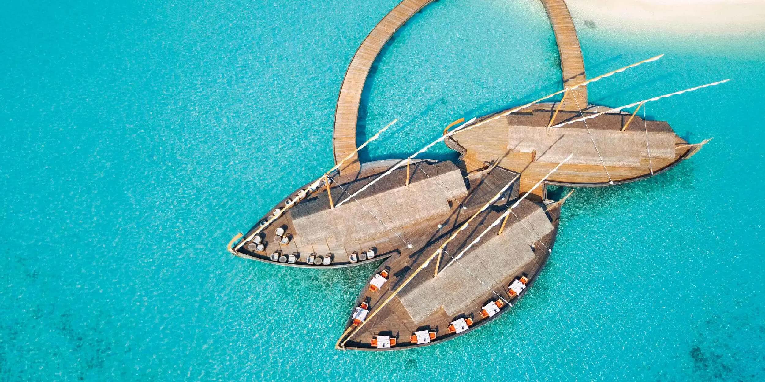 Milaidhoo's 300-by-180-metre island seen from the air, overwater villas tracing the reef edge.