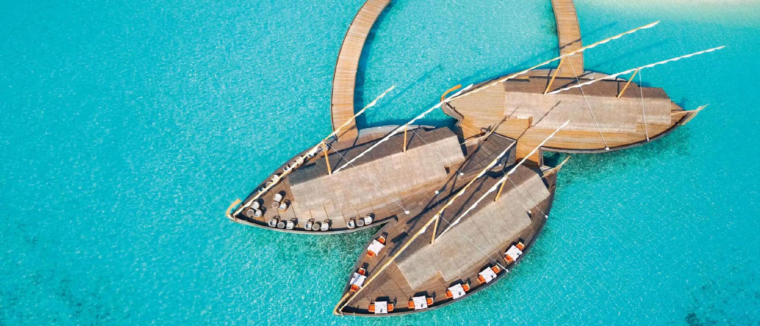 Milaidhoo's 300-by-180-metre island seen from the air, overwater villas tracing the reef edge.
