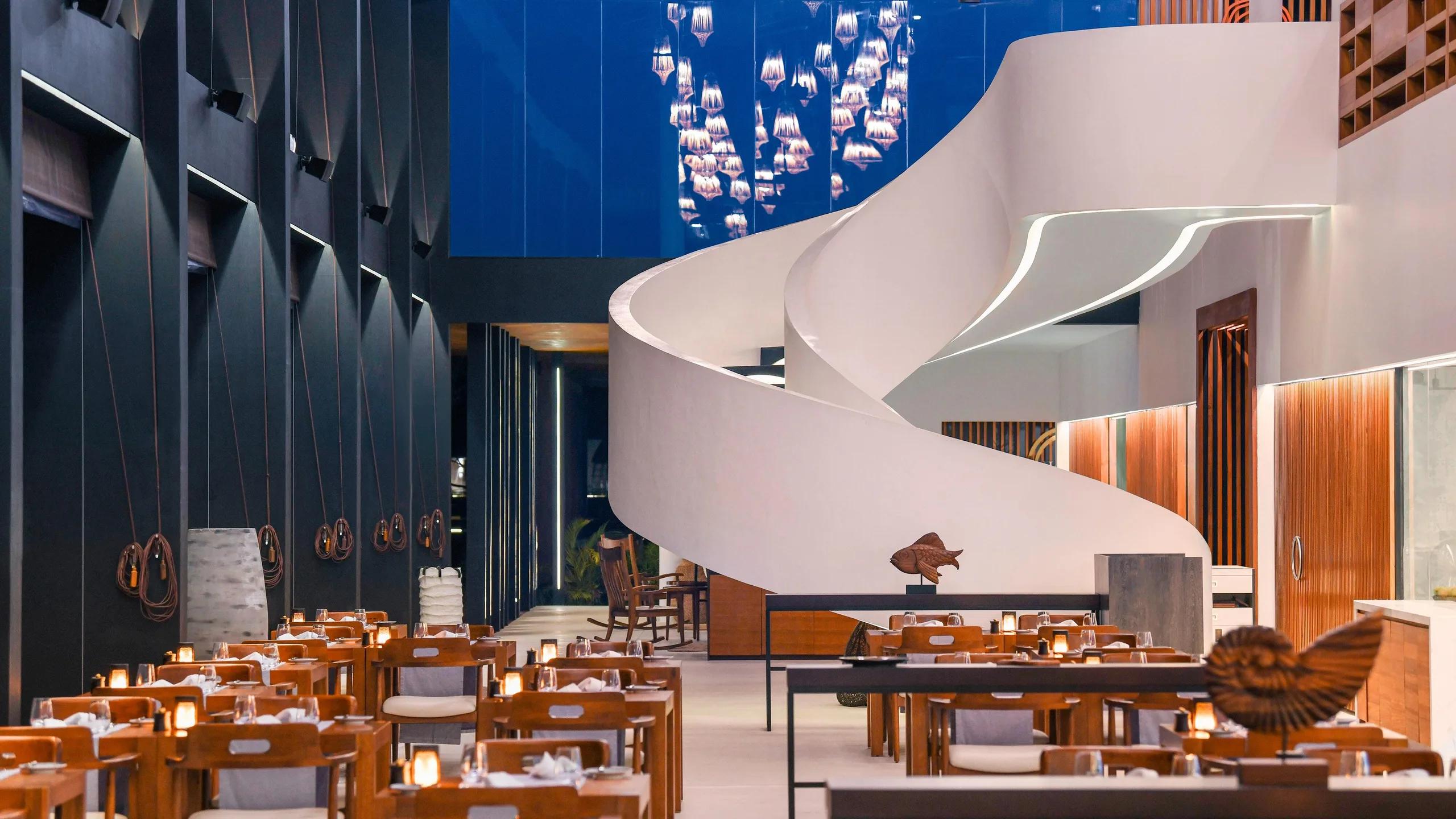 A sculptural white staircase connecting Island Kitchen's dining levels, lanterns hanging above