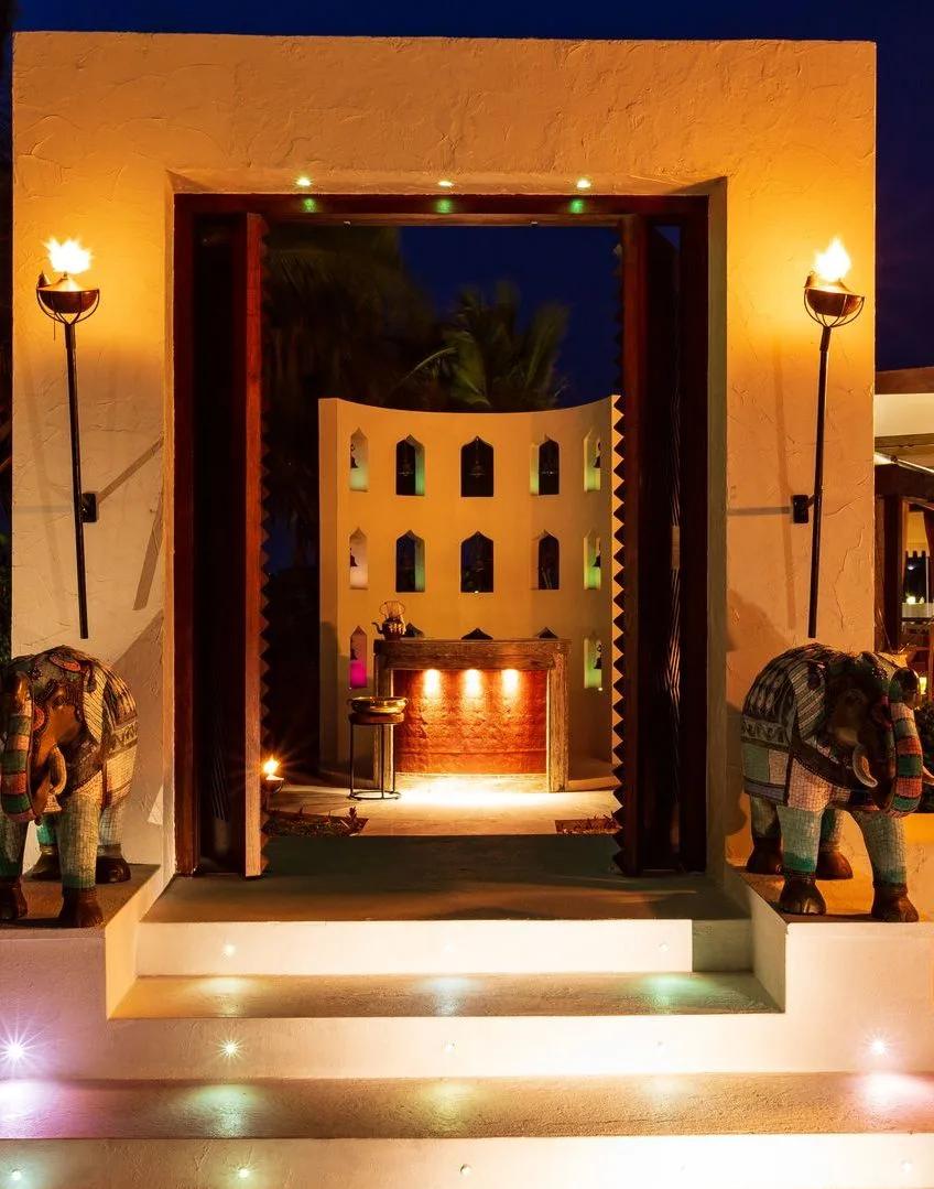 Saffron restaurant's torch-lit entrance at night, flanked by carved elephant statues and an illuminated spice-bottle wall
