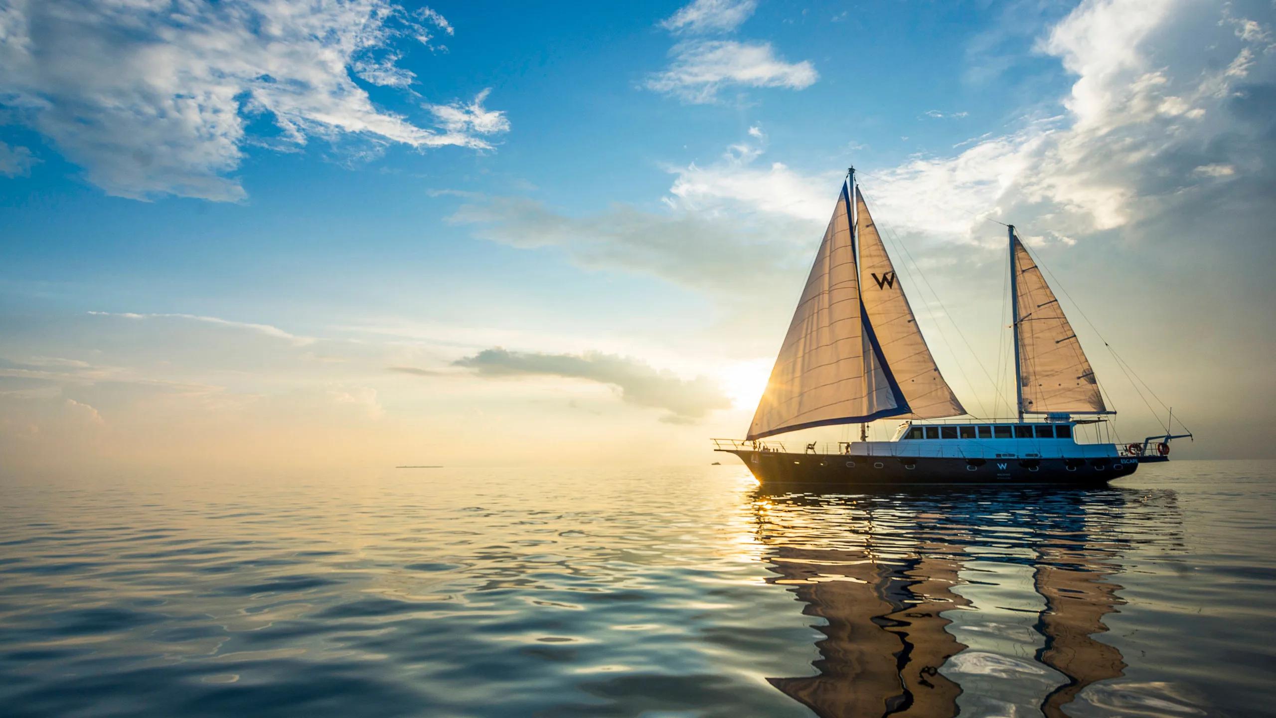 W Maldives' own sailing yacht under sail, its white sails catching the light against a pale sky