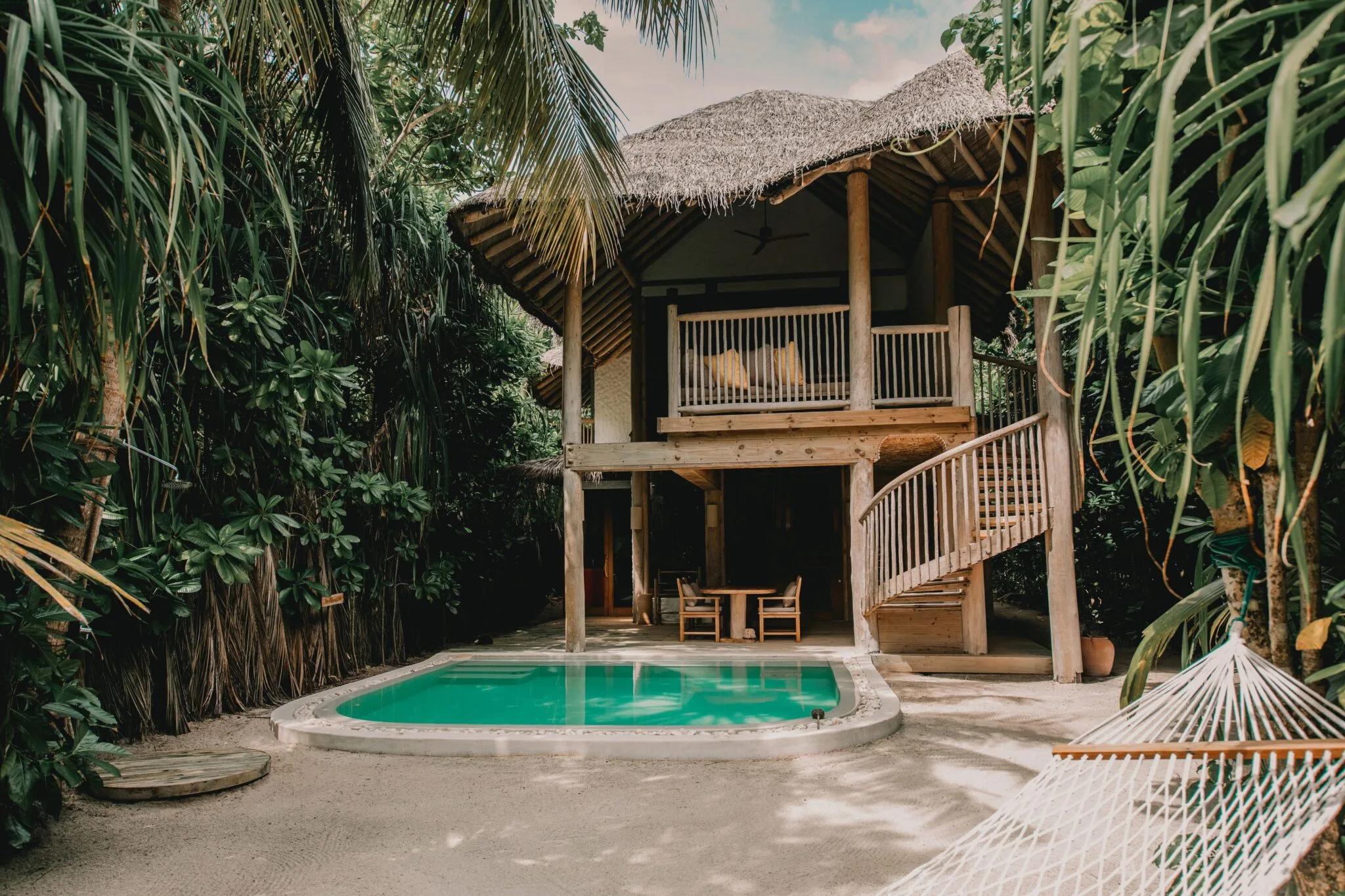 A two-storey thatched-roof Crusoe Suite with its private pool set in a jungle clearing, a spiral staircase leading to the upper deck and a hammock strung between the palms
