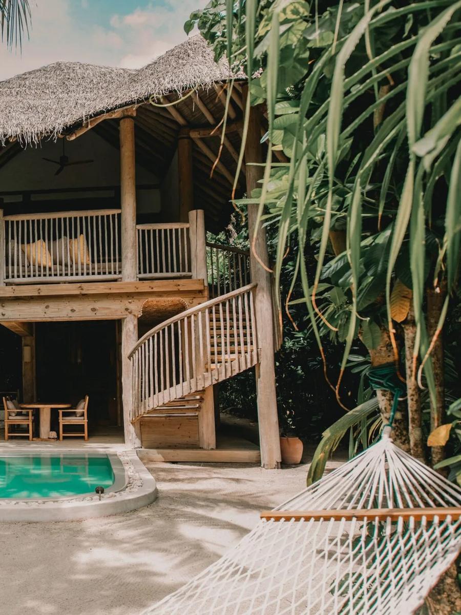 A two-storey thatched-roof Crusoe Suite with its private pool set in a jungle clearing, a spiral staircase leading to the upper deck and a hammock strung between the palms