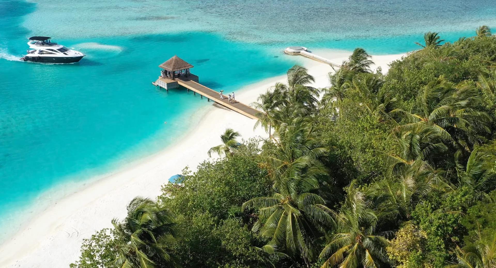 A boat arriving at Naladhu's overwater arrival jetty, a thatched pavilion on stilts with a sandbank runway beyond