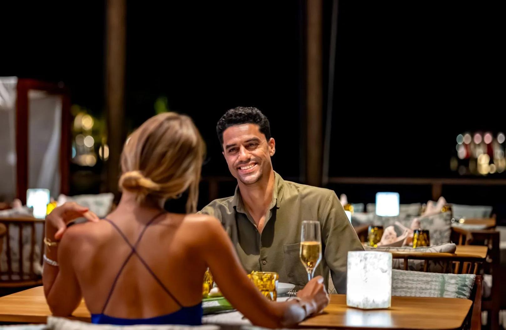 A couple at a candlelit table after dark, champagne poured, the restaurant's open-air seating behind them