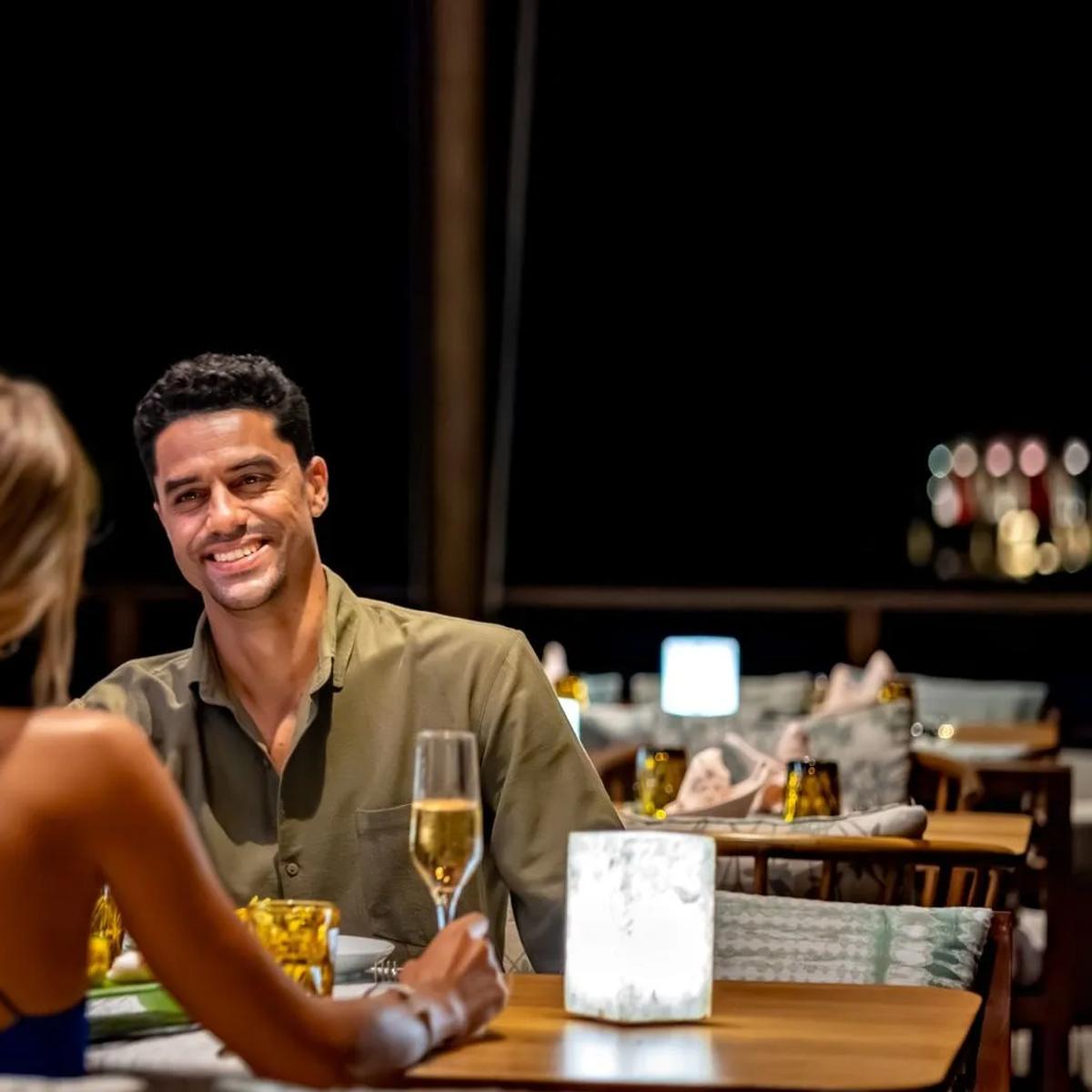 A couple at a candlelit table after dark, champagne poured, the restaurant's open-air seating behind them
