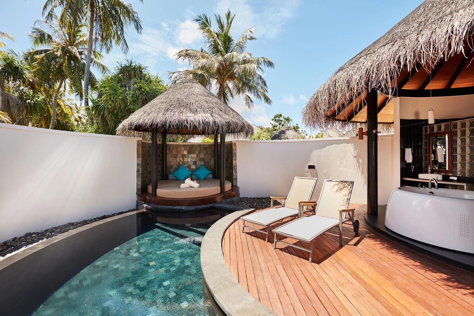 A curved private pool beside a thatched daybed cabana with teal cushions, palm trees framing the walled garden of a Beach Villa with Pool