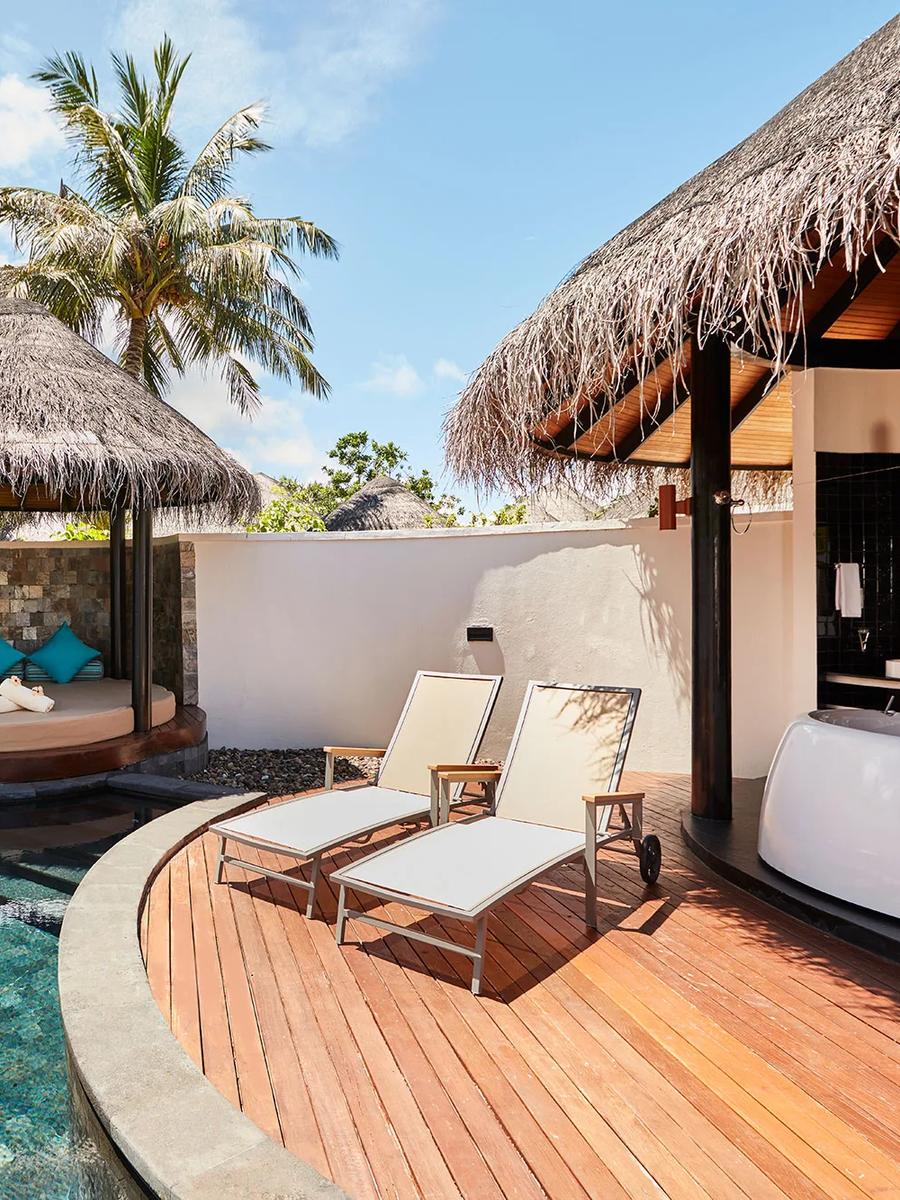 A curved private pool beside a thatched daybed cabana with teal cushions, palm trees framing the walled garden of a Beach Villa with Pool