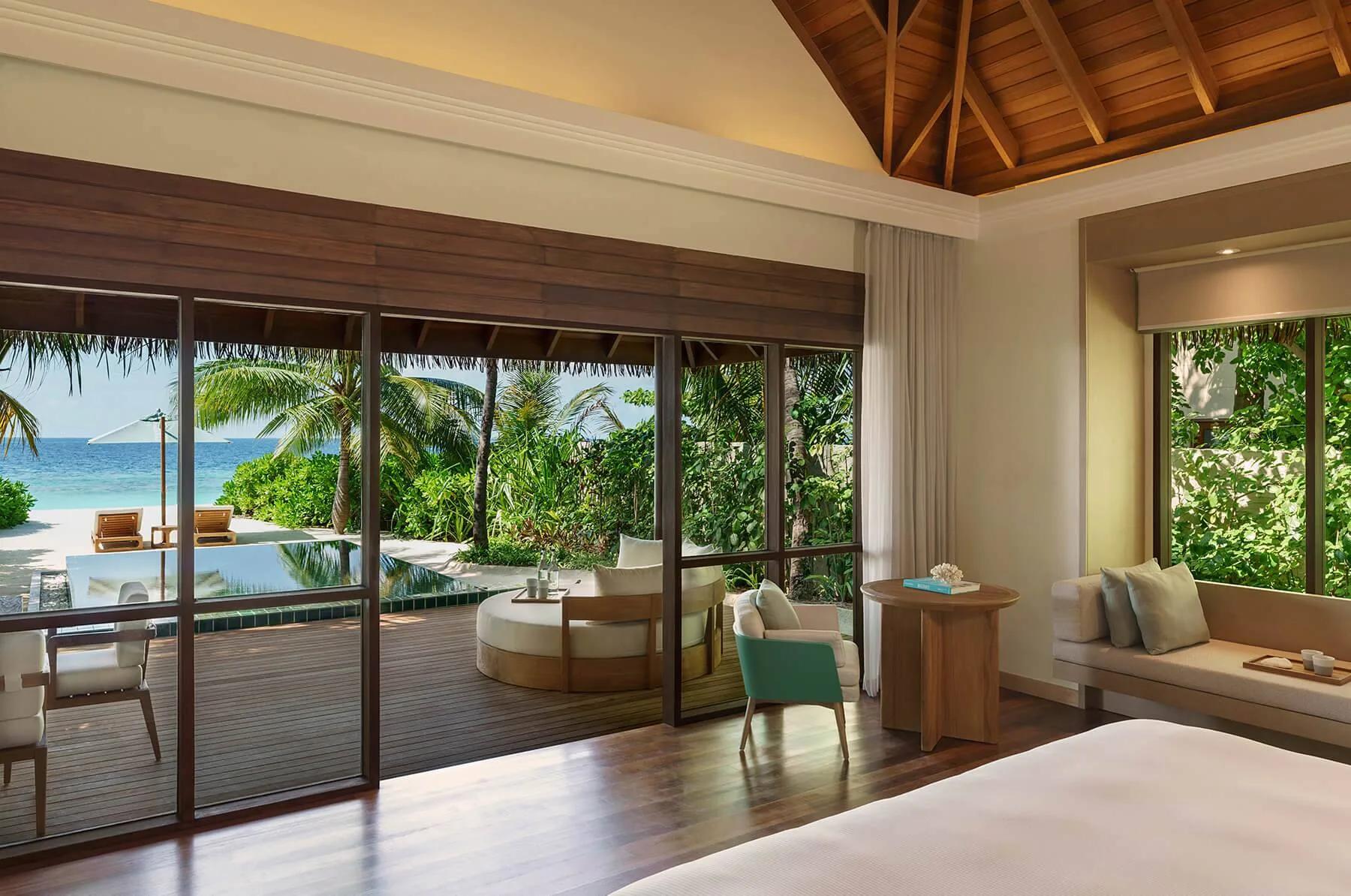 The bedroom of a Deluxe Beach Bungalow with Pool, glass doors open to its private pool and the beach beyond