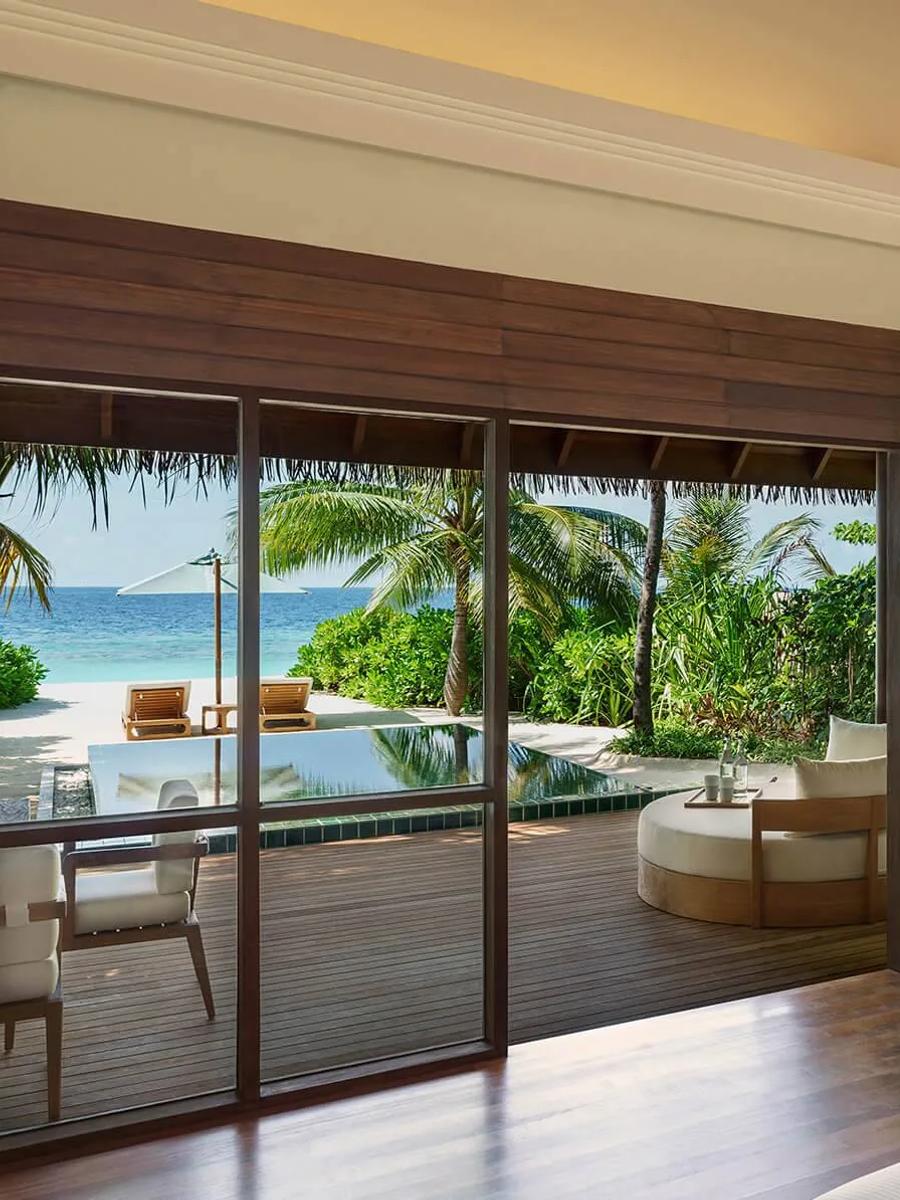 The bedroom of a Deluxe Beach Bungalow with Pool, glass doors open to its private pool and the beach beyond