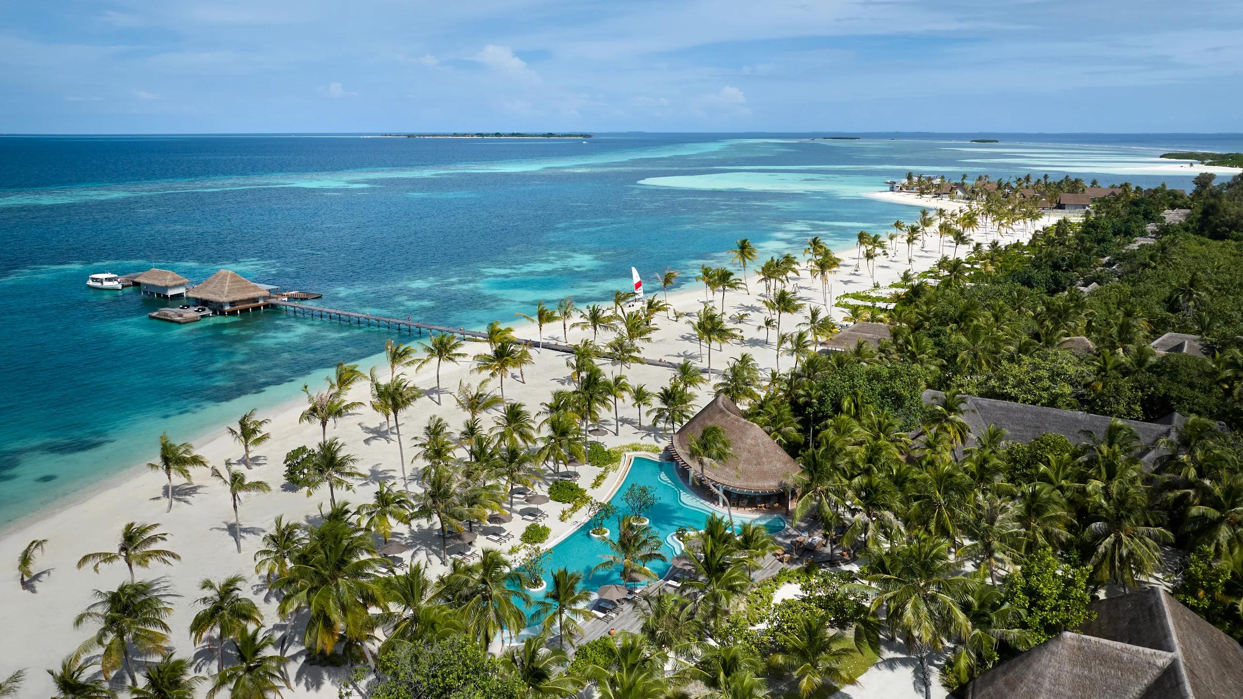 Aerial view of a beachfront pool and jetty near Sip & Sand, with a catamaran sailing offshore.
