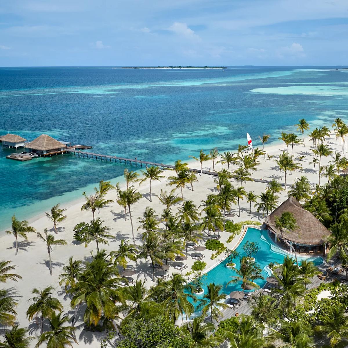 Aerial view of a beachfront pool and jetty near Sip & Sand, with a catamaran sailing offshore.